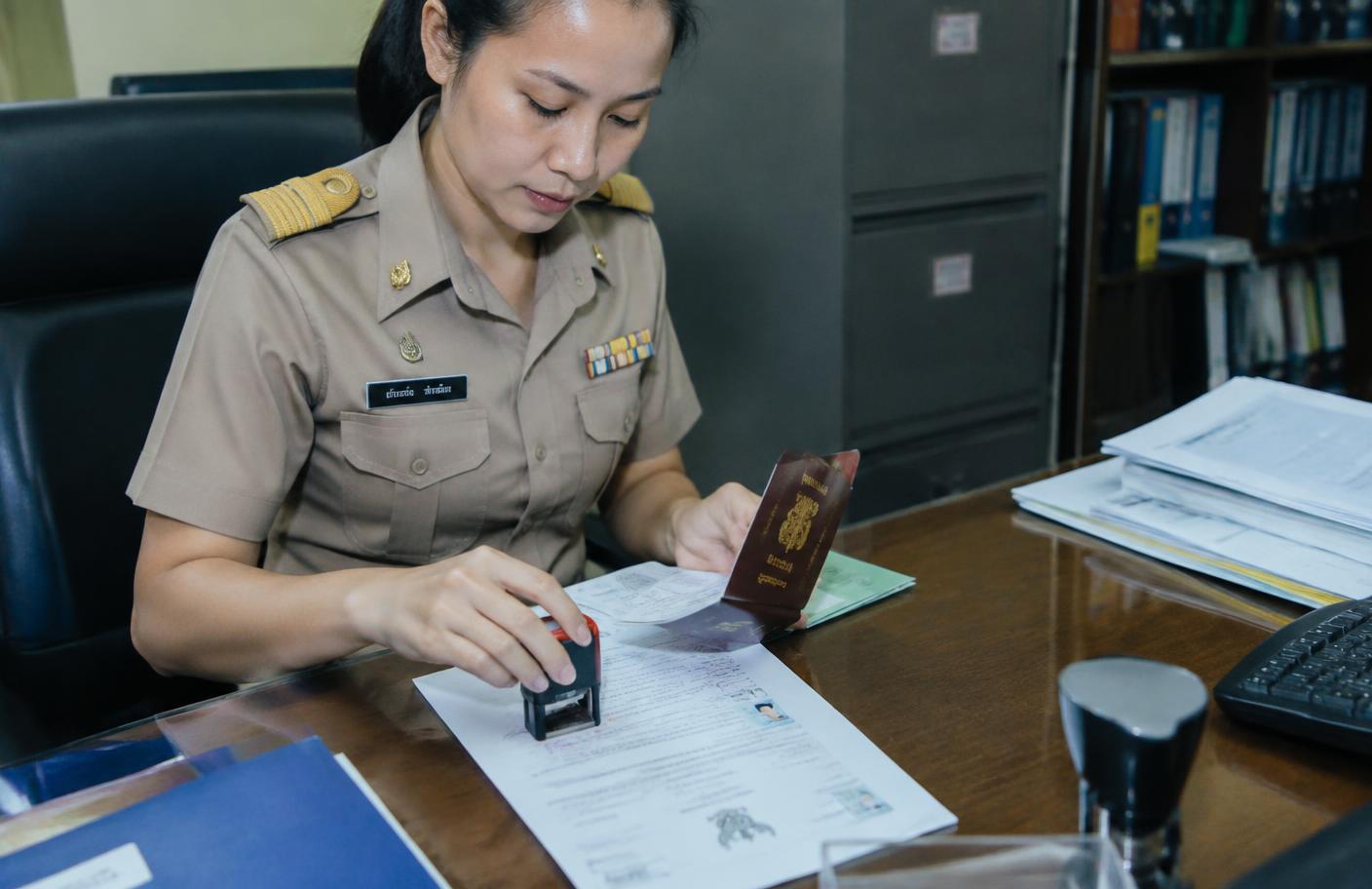 เจ้าหน้าที่เทียบหนังสือเดินทางต้นฉบับกับสำเนาแล้วประทับตรารับรอง